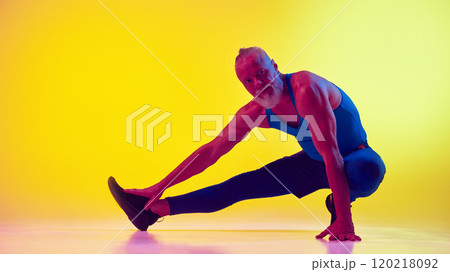 Elderly man with muscular strong body, in sportswear training, doing stretching exercises against gradient yellow background in neon light Elderly man with muscular strong body, in sportswear training, doing stretching exercises against gradient yellow background in neon light 120218092
