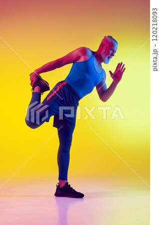 Athletic elderly man in sportswear balancing on one leg, training against gradient yellow background in neon light Athletic elderly man in sportswear balancing on one leg, training against gradient yellow background in neon light 120218093