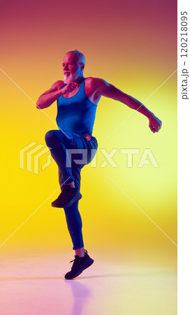 Full-length dynamic image of muscular elderly man in sportswear in motion, training against gradient yellow background in neon light Full-length dynamic image of muscular elderly man in sportswear in motion, training against gradient yellow background in neon light 120218095