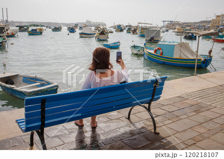 Woman traveler taking pictures in touristic fishing village Marsaxlokk in Malta 120218107