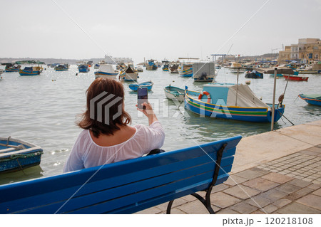 Woman traveler taking phone pictures in touristic fishing village Marsaxlokk in Malta 120218108