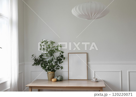 Elegant Scandinavian living room interior, home office. Wooden poster, picture frame mockup on table. Green branches in vase, pumpkins, cup of coffee. Textile lamp shade. Thanksgiving home decor. Elegant Scandinavian living room interior, home office. Wooden poster, picture frame mockup on table. Green branches in vase, pumpkins, cup of coffee. Textile lamp shade. Thanksgiving home decor. 120220071