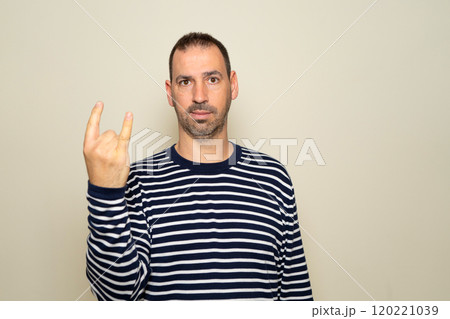 Portrait of bearded man showing rock and roll gesture, heavy metal sign, exclaiming with joy. Indoor studio photo isolated on beige background. Portrait of bearded man showing rock and roll gesture, heavy metal sign, exclaiming with joy. Indoor studio photo isolated on beige background. 120221039