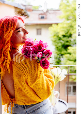 Young Caucasian woman n yellow sweater with orange hair embraces pink flower bouquet on balcony. Greenery and bright colors, joy and romance. Vibrant lifestyle concept. Young Caucasian woman n yellow sweater with orange hair embraces pink flower bouquet on balcony. Greenery and bright colors, joy and romance. Vibrant lifestyle concept. 120222203