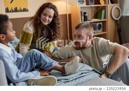 Medium shot of emotionally supportive parents talking to adopted Black boy while sitting in bed during important conversation in kids room 120223956