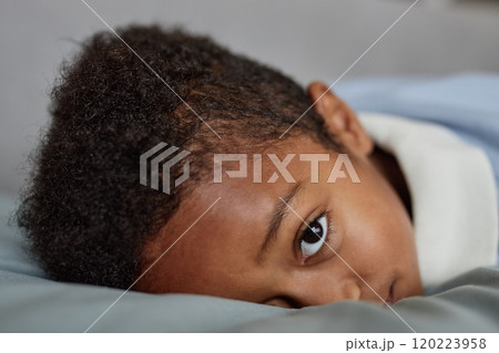Close up of little Black boy looking at camera with expression of curiosity on face while lying down on bed at home, copy space Close up of little Black boy looking at camera with expression of curiosity on face while lying down on bed at home, copy space 120223958