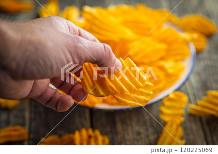 A hand taking a potato chip from a bowl. 120225069