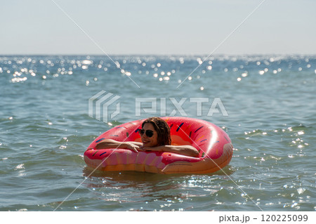 Woman Watermelon Float Summer Beach - A woman floats on a watermelon-shaped raft in the ocean on a sunny summer day. 120225099