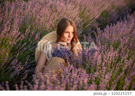 A woman is sitting in a field of lavender flowers. She is wearing a straw hat and holding a basket of flowers. The scene is peaceful and serene, with the woman enjoying the beauty of the flowers. 120225157