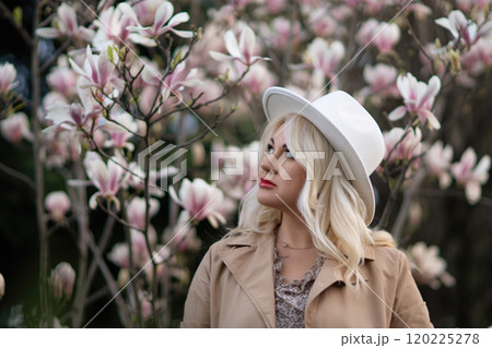 A blonde woman wearing a white hat stands in front of a tree with pink flowers 120225278