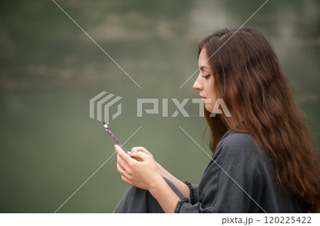 A woman is talking on her cell phone while sitting on a dock. She is wearing a black jacket and she is in a relaxed mood. A woman is talking on her cell phone while sitting on a dock. She is wearing a black jacket and she is in a relaxed mood. 120225422