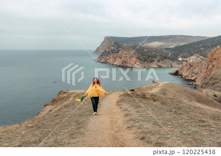 A woman is walking on a path near the ocean. She is carrying a bouquet of flowers. 120225438