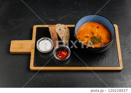 Hearty soup with bread, sour cream, and chili peppers on a slate board for a cozy meal 120228837