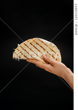 Grilled tortilla wrap with fresh filling held in hand, a perfect grab-and-go snack or lunch option Grilled tortilla wrap with fresh filling held in hand, a perfect grab-and-go snack or lunch option 120228857