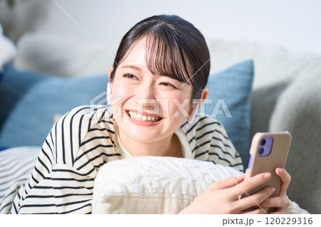 ソファーに寝そべる私服の若い女性　リビング　スマホ 120229316