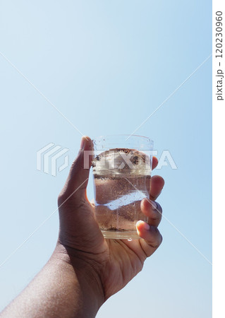 holding dirty glass of water against blue sky  120230960