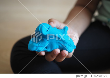 A childs small hand is holding a piece of bright blue modeling clay with enjoyment A childs small hand is holding a piece of bright blue modeling clay with enjoyment 120230979