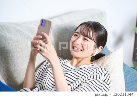 ソファーに寝そべる私服の若い女性　リビング　スマホ 120231344