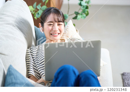 ソファーに寝そべる私服の若い女性　リビング　スマホ 120231348