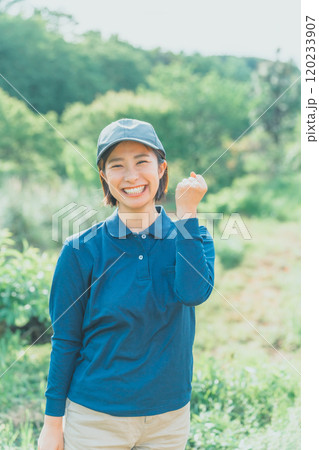 青いポロシャツ姿の若い女性が緑豊かな自然の中でガッツポーズをしている 120233907