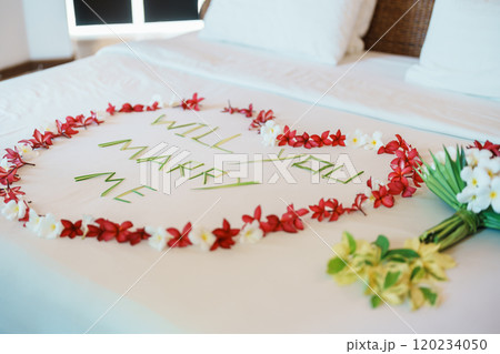 message WILL YOU MARRY ME made of flower petals with bouquet and Heart shape on bed. Idea for marriage proposal, romantic surprise, wedding and engagement concept 120234050