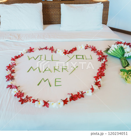 message WILL YOU MARRY ME made of flower petals with bouquet and Heart shape on bed. Idea for marriage proposal, romantic surprise, wedding and engagement concept 120234051