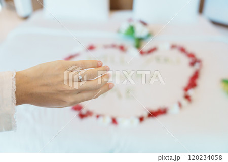 Woman hand wearing a diamond ring after say YES with message WILL YOU MARRY ME made of flower petals with bouquet on bed. Idea for marriage proposal, romantic surprise, wedding and engagement concept 120234058