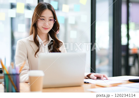 Professional focused on laptop with paperwork for business tasks Professional focused on laptop with paperwork for business tasks 120234114