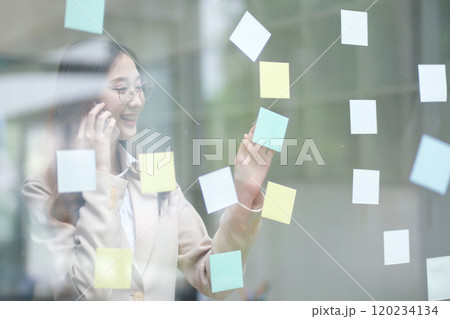 Businesswoman writing on sticky notes while planning business strategy 120234134