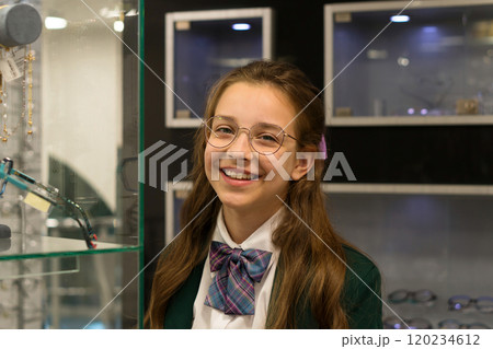 Girl in optical shop, standing next to display of glasses 120234612