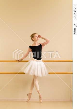 Focused ballerina stands gracefully on pointe, holding barre 120234798