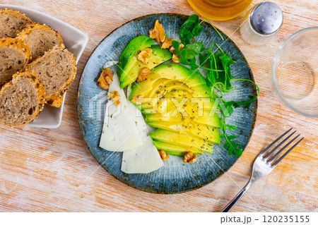 On table there is plate with snack - pieces of avocado pulp, walnut and arugula. 120235155