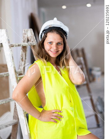 Sexy young woman in a yellow vest and protective helmet poses playfully in renovated room Sexy young woman in a yellow vest and protective helmet poses playfully in renovated room 120235691