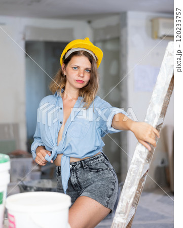 Sexy woman in denim shirt and shorts next to a stepladder in room being renovated 120235757