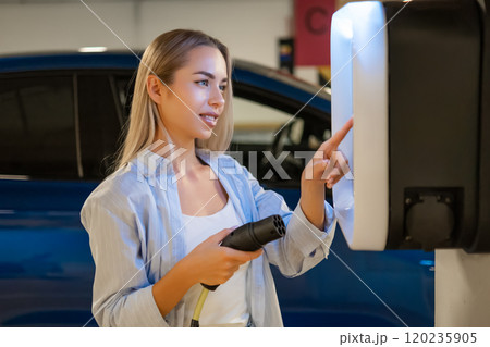 Woman is using a charging station for her electric vehicle in a parking garage Woman is using a charging station for her electric vehicle in a parking garage 120235905