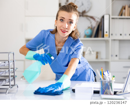 Positive woman cleaner polishing table in office 120236147