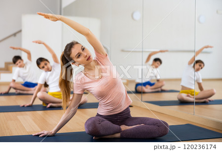 Young woman with teenage kids doing stretching in Padmasana pose in yoga studio Young woman with teenage kids doing stretching in Padmasana pose in yoga studio 120236174