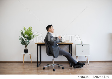 Asian businessman relaxing with coffee in modern office setting 120236189
