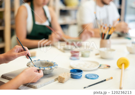 Girl hands paints bowl of clay during master class, close up 120236213