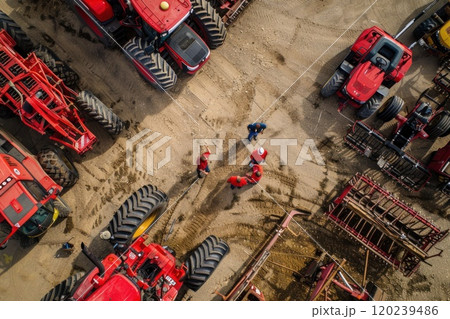 An aerial view of four red tractors parked in a lot with four people standing near the center. An aerial view of four red tractors parked in a lot with four people standing near the center. 120239486