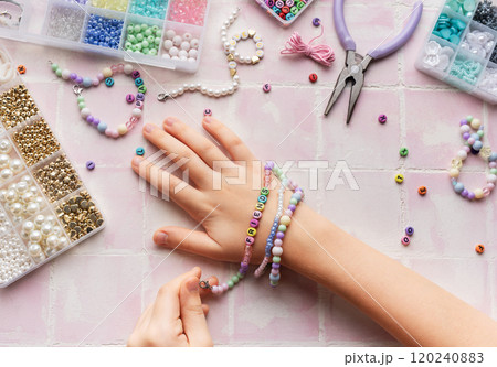 Child making beaded bracelets at home on pink tiled table Child making beaded bracelets at home on pink tiled table 120240883