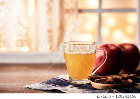木のテーブルの上にホットアップルサイダー、窓にはクリスマスライト 120242156