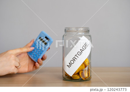 Bank of coins Mortgage and hand with calculator. The accumulation of money to pay interest rates on mortgages. Buying a property in debt. Take credit for housing. Mortgage tax and loan concept. 120243773