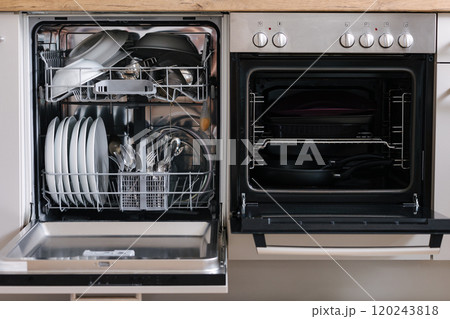 Open dishwasher placed beside an oven. Dishwasher loaded with clean dishes. Empty oven Open dishwasher placed beside an oven. Dishwasher loaded with clean dishes. Empty oven 120243818