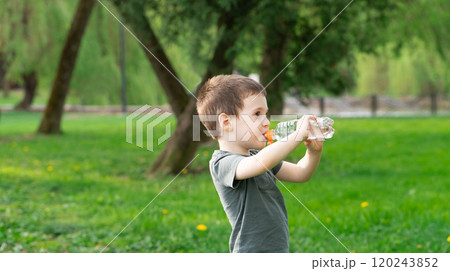 Three year old caucasian toddler boy drinks water from a bottle in the park on a spring or summer day. 120243852