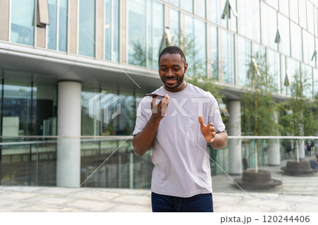 African american man talking on smartphone on street in city outdoor. Man with cell phone chatting with friends. Smiling person making answering call by cellphone. Guy having conversation by mobile 120244406
