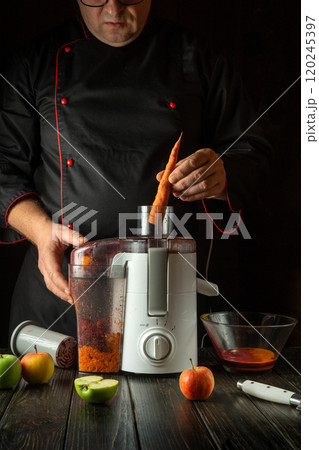 Chef manually adding raw carrots to electric juicer. Making healthy vegetable juice on hotel kitchen counter for breakfast Chef manually adding raw carrots to electric juicer. Making healthy vegetable juice on hotel kitchen counter for breakfast 120245397
