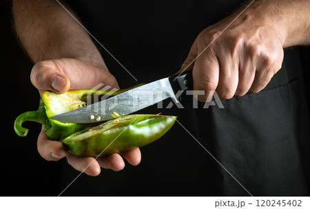 A pair of hands skillfully slices through a vibrant green pepper, showcasing its juicy interior. The focus is on the artistry of food preparation under soft kitchen lighting A pair of hands skillfully slices through a vibrant green pepper, showcasing its juicy interior. The focus is on the artistry of food preparation under soft kitchen lighting 120245402