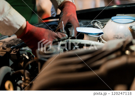 Mechanic Performing Maintenance on a Car Engine Under Dim Lighting 120247118