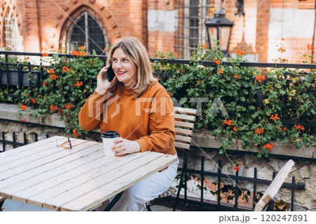Young charming woman calling with cell telephone while sitting alone on cafe terrace. Female having conversation on mobile phone while rest in cafe Young charming woman calling with cell telephone while sitting alone on cafe terrace. Female having conversation on mobile phone while rest in cafe 120247891